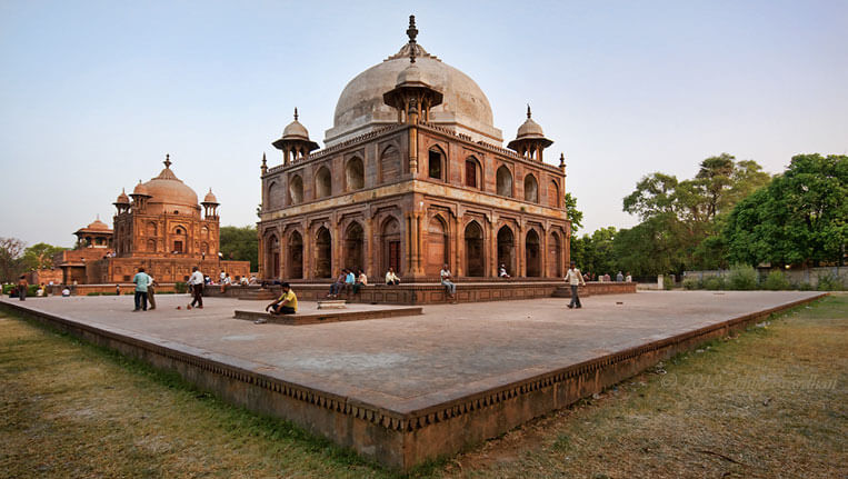 Visitors at a historical Mughal era tomb complex in Allahabad during sunset.